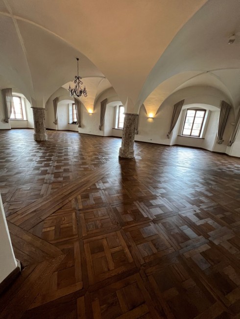 Gro&szlig;er Raum mit Holzboden, gew&ouml;lbter Decke, Kronleuchter und Fenstern mit Vorh&auml;ngen