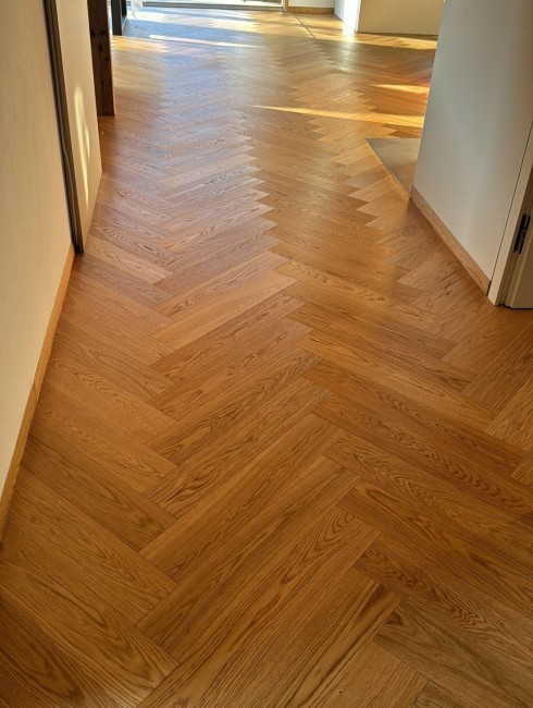 Heller holzfarbener Chevron-Parkettboden in einem sonnendurchfluteten Flur